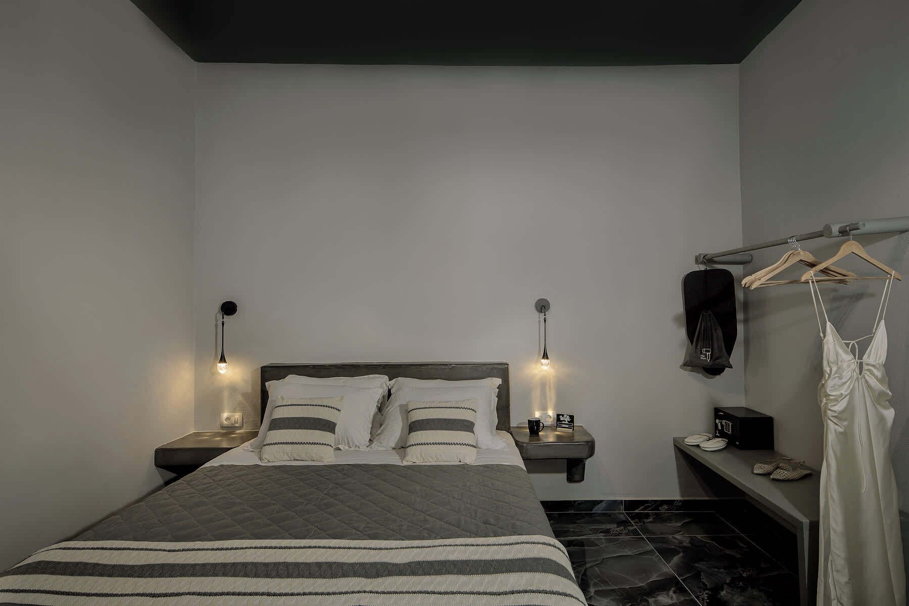 A bedroom with a bed, bedside tables, a hanging garment, and a wall-mounted shelf.