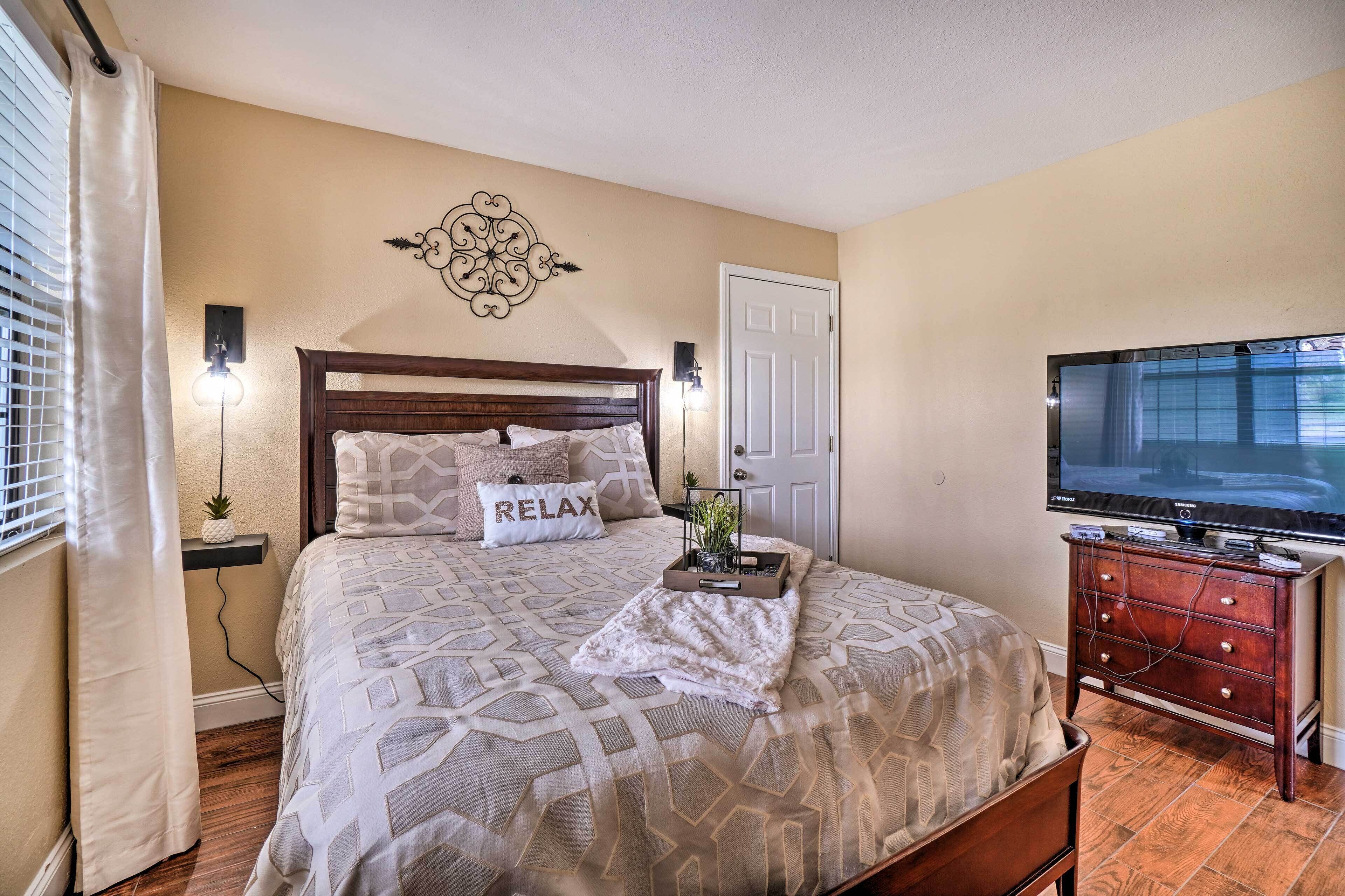 A neatly arranged bedroom with a bed, a TV, a dresser, and a decorative wall piece.