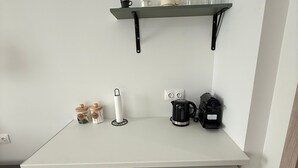 A kitchenette with a white countertop, a green cabinet, a white refrigerator, a black coffee maker, a white kettle, and a shelf with cups and a glass. - Athenian Stay 304 Monastiraki (Athens)
