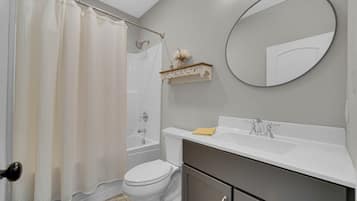 A bathroom with a shower curtain, toilet, bathtub, sink, mirror, and a shelf with a vase.