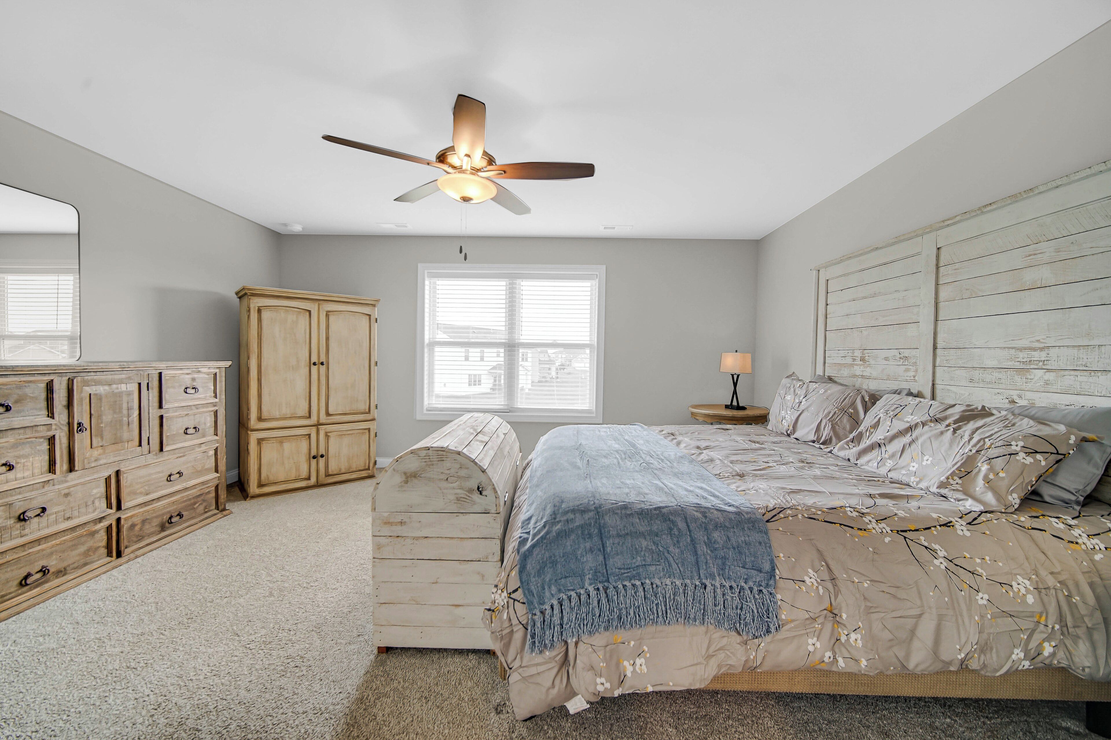 A bedroom with a bed, a ceiling fan, a wardrobe, a dresser, and a window.