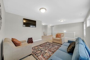 Un salon avec un canapé, un fauteuil et un téléviseur fixé au mur.