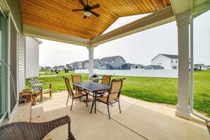 Une terrasse couverte avec une table et des chaises, un ventilateur de plafond et une vue sur les maisons au loin.