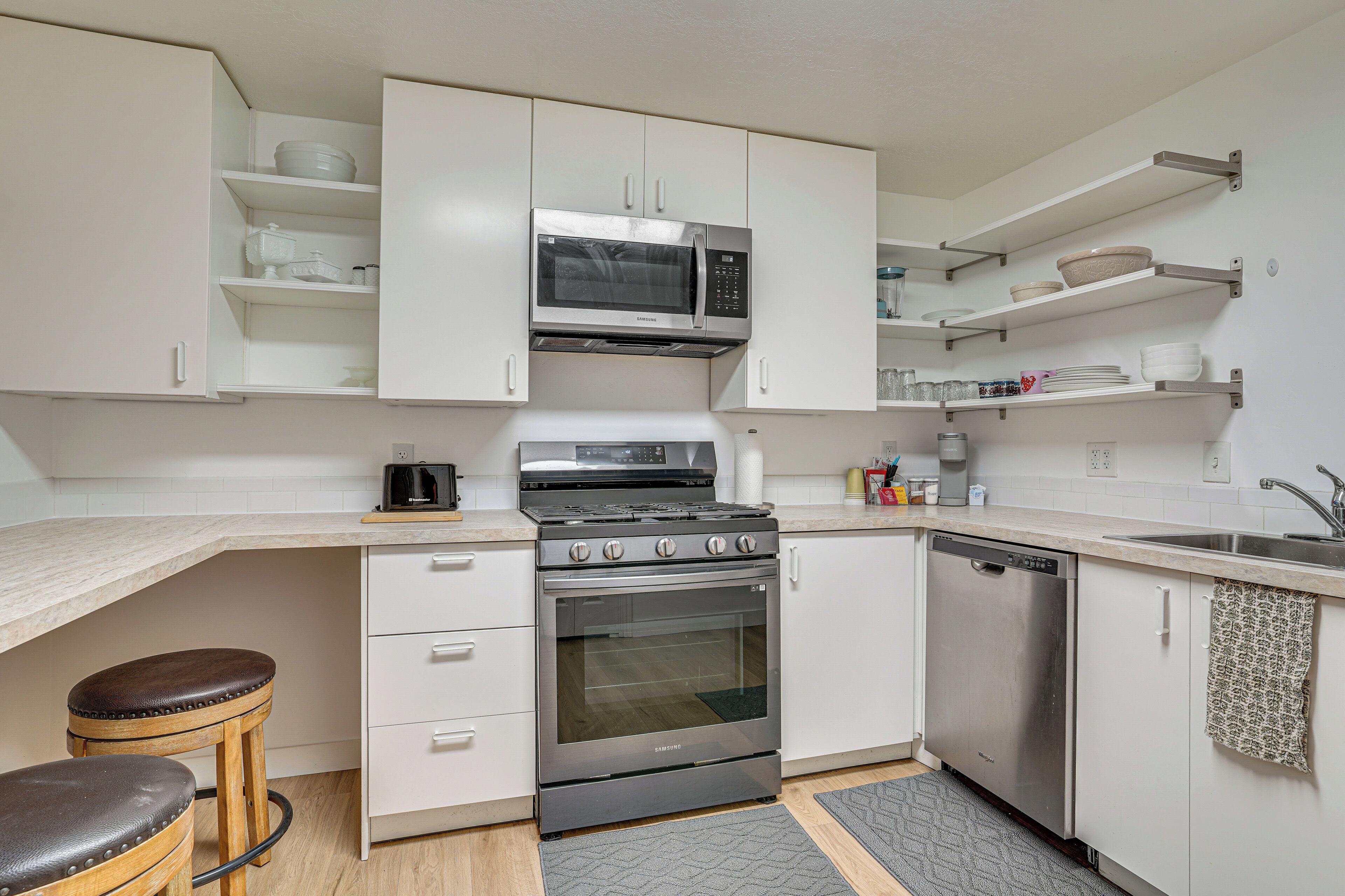 Una cocina con gabinetes blancos, estufa de acero inoxidable, microondas y lavavajillas.