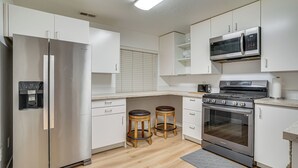 Una cocina moderna con electrodomésticos de acero inoxidable, taburetes de madera y armarios blancos.