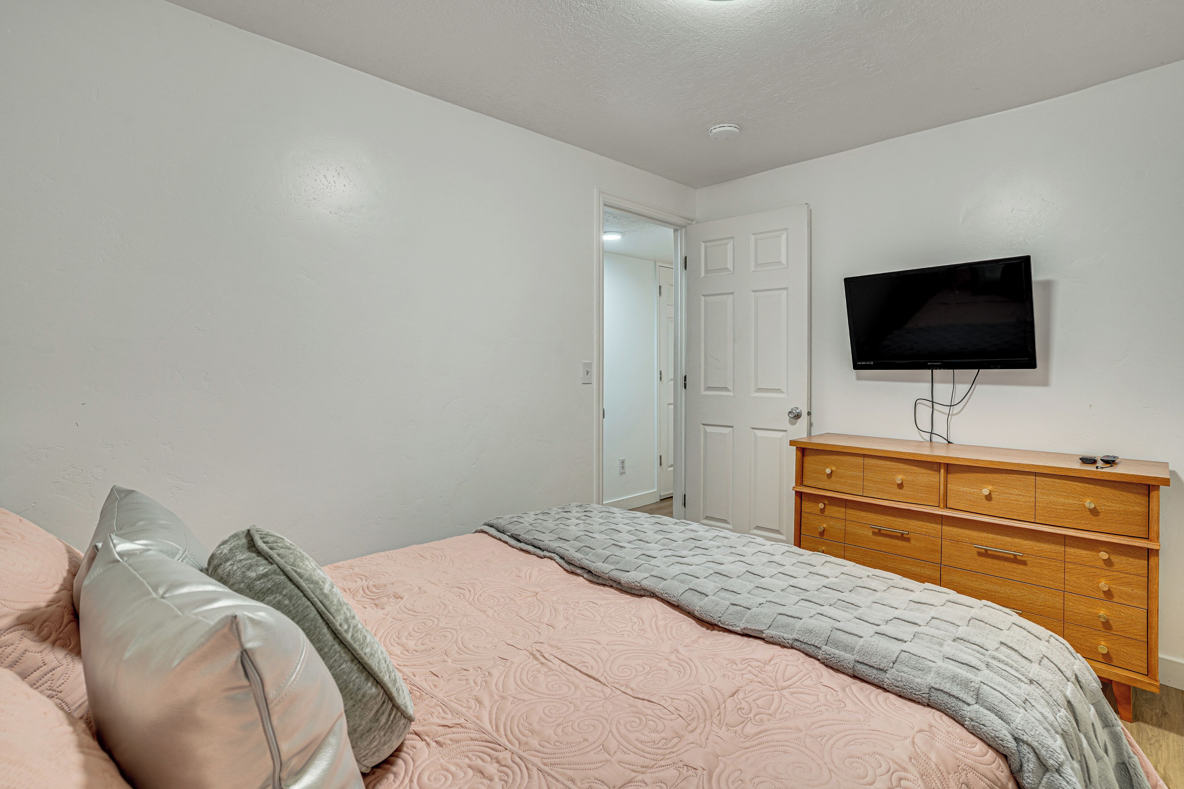 Une chambre à coucher comprenant un lit, une commode, un téléviseur et une porte donnant sur une autre pièce.