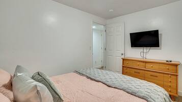 Une chambre à coucher comprenant un lit, une commode, un téléviseur et une porte donnant sur une autre pièce.