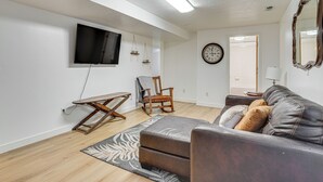 Una sala de estar con un sofá, una silla, un televisor, un reloj y una lámpara.