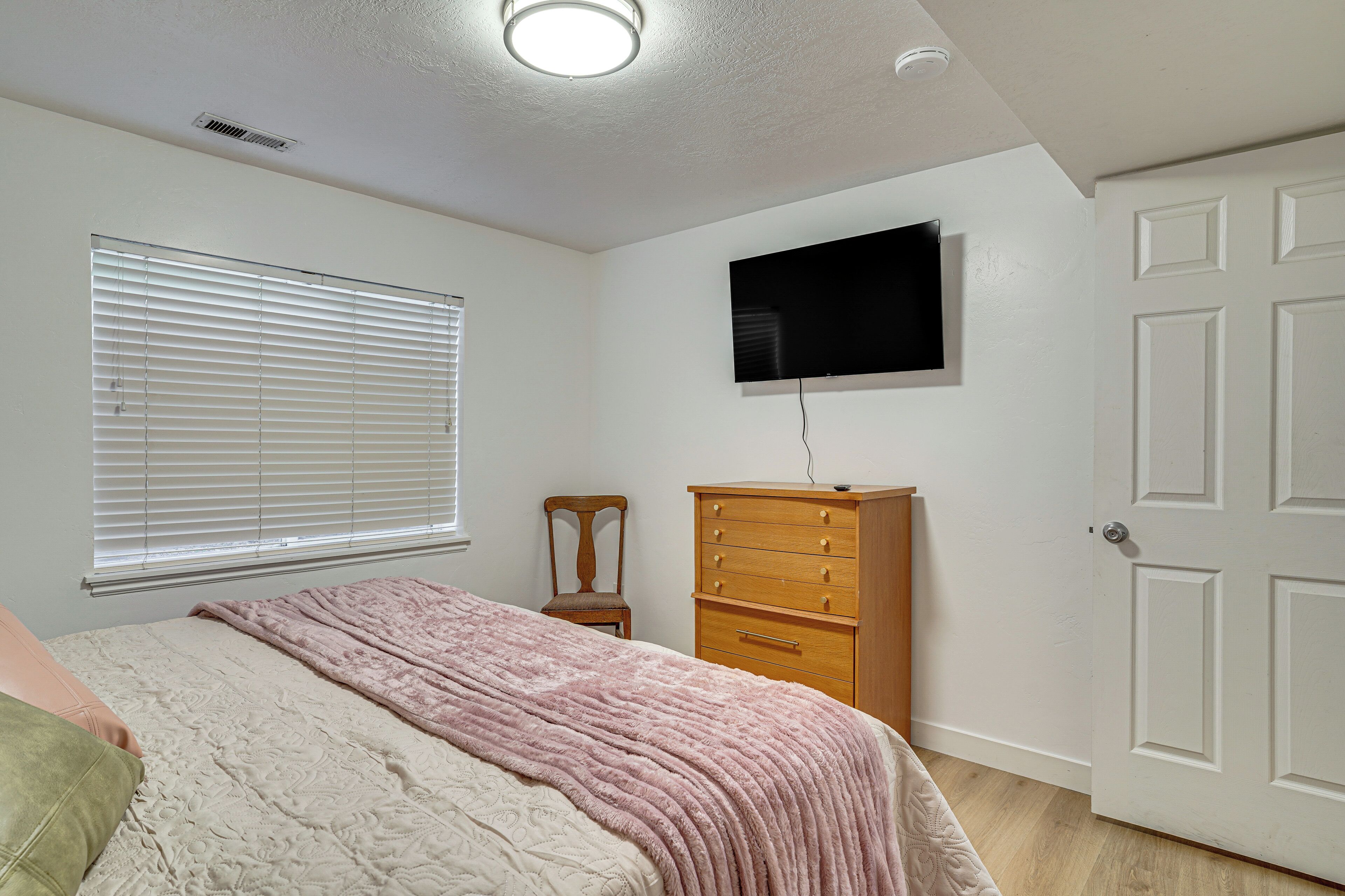 A bedroom with a bed, a dresser, a chair, a television, and a door.