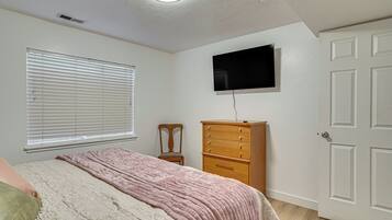 A bedroom with a bed, a dresser, a chair, a television, and a door.