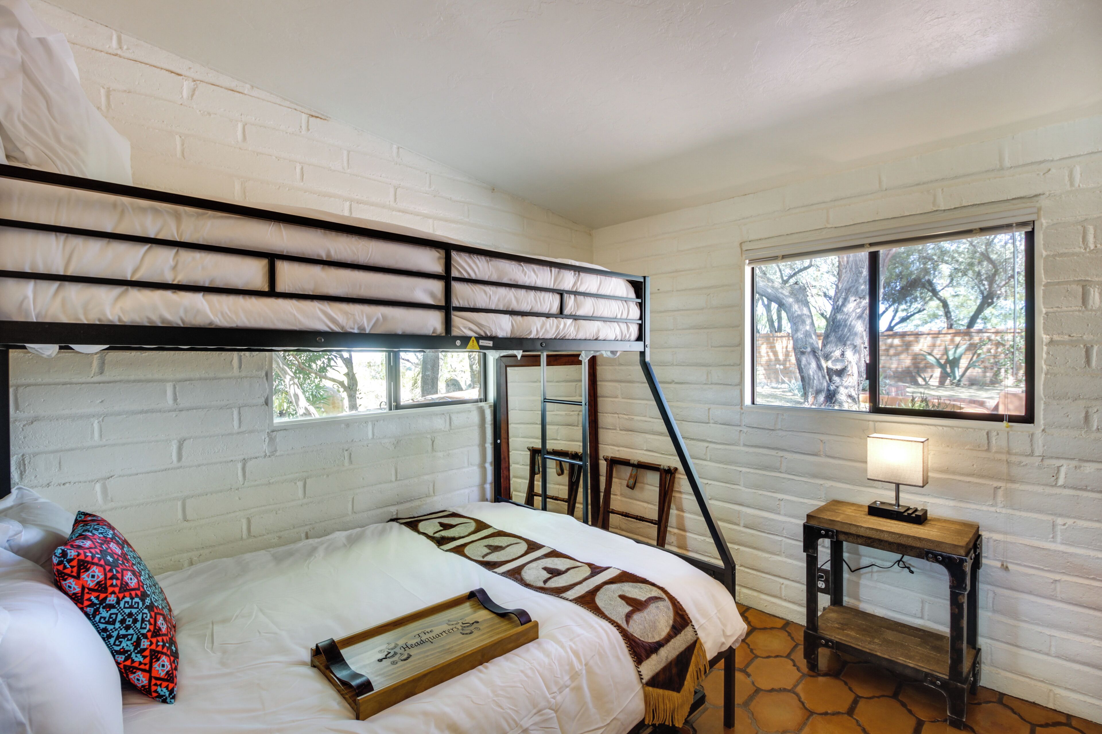 A bunk bed with a ladder, a bedside table with a lamp, and a window with a view of trees.