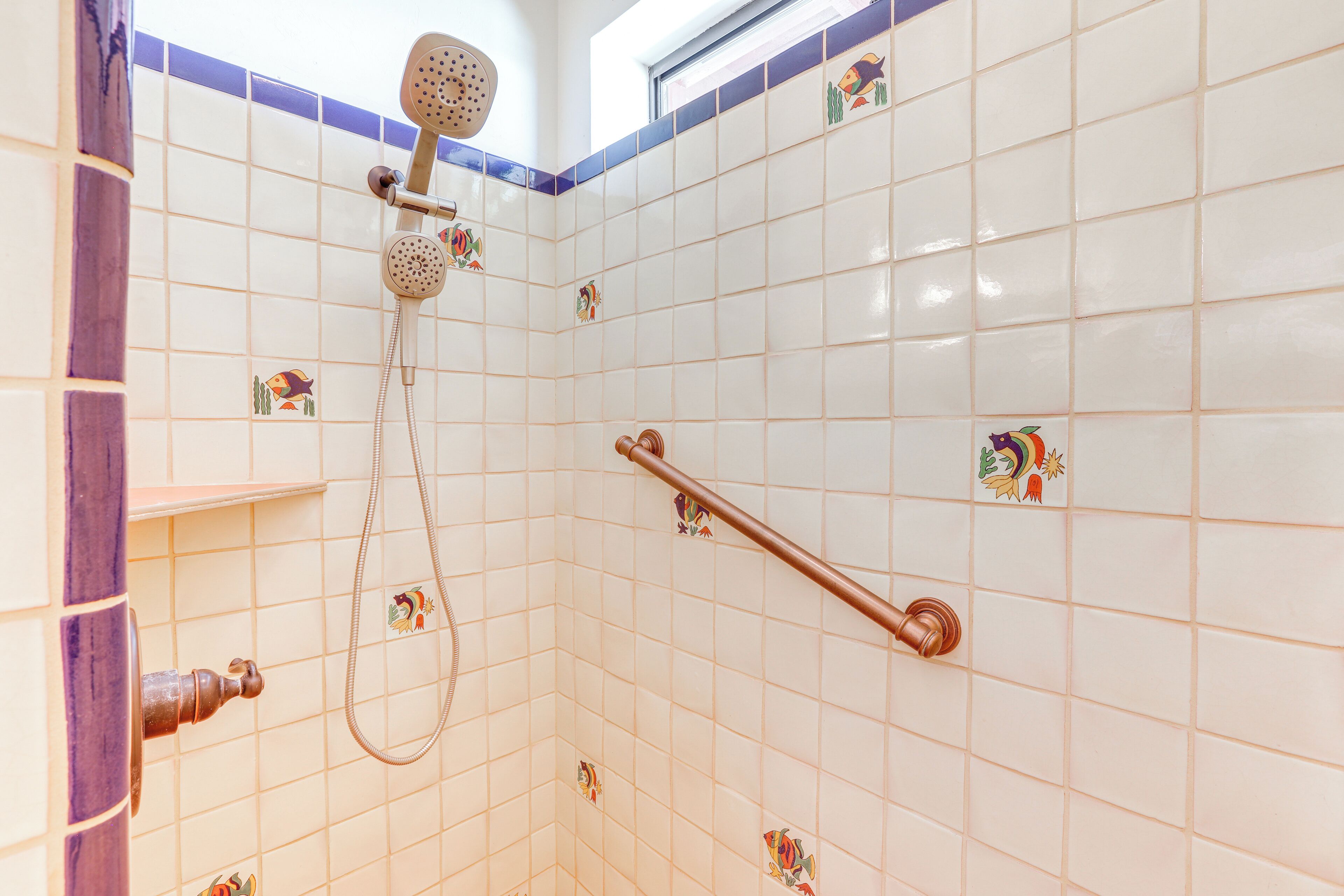 Une zone de douche carrelée, équipée d’un pommeau de douche à main, d’un pommeau de douche fixé au mur et d’une barre d’appui.