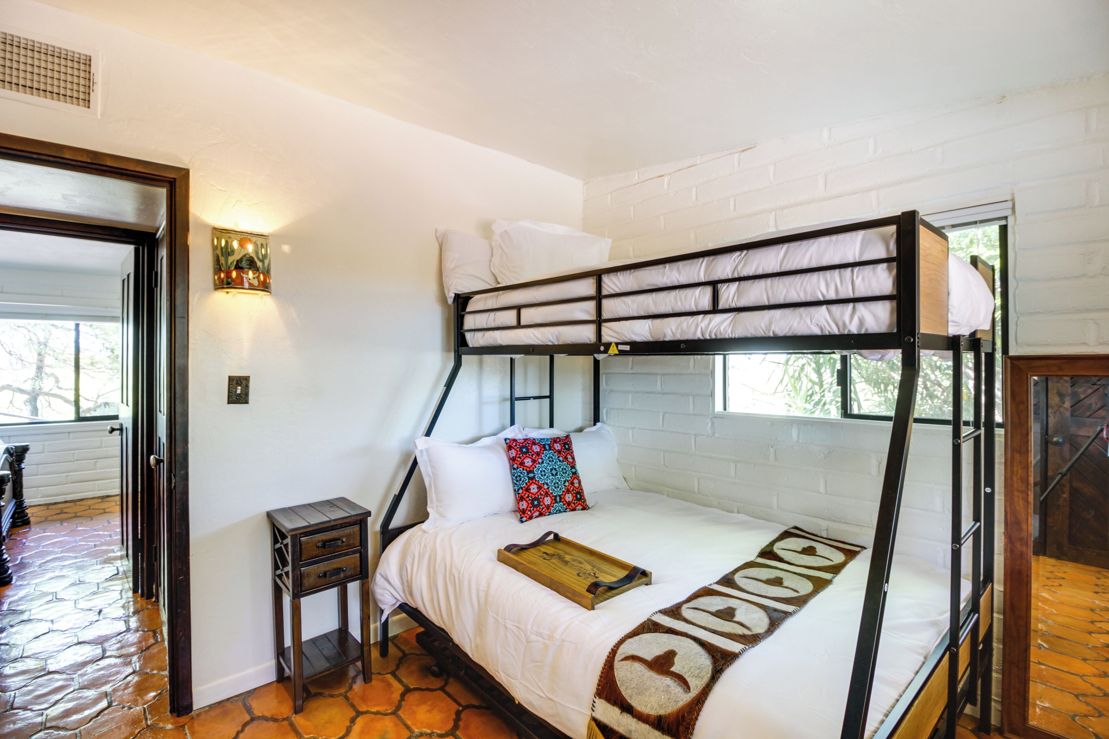 A bunk bed with a wooden headboard, white bedding, and a small bedside table with drawers.