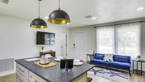 Una cocina moderna con encimeras de granito, una isla central, iluminación colgante y un área de comedor con un sofá azul y una mesita auxiliar.