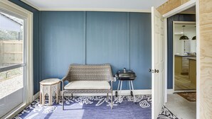 Una habitación con pared azul, alfombra estampada, sofá de mimbre, un taburete pequeño y una parrilla.