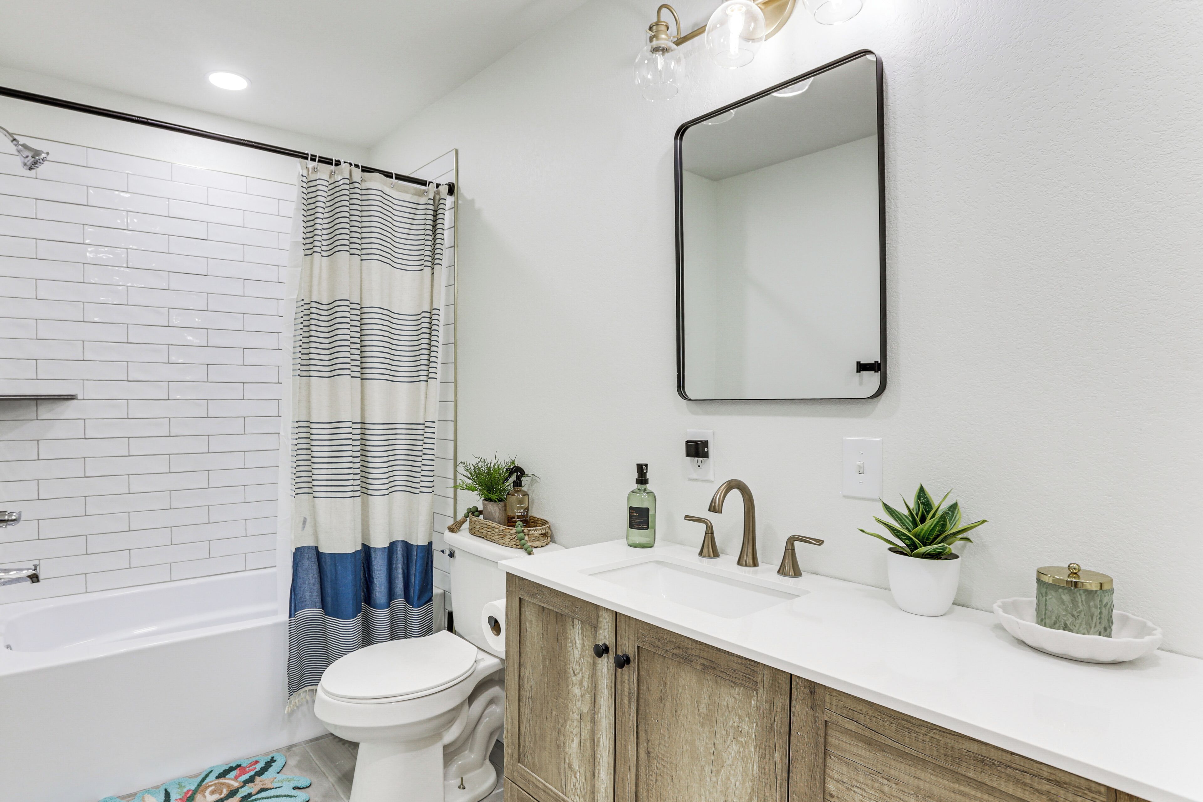 A bathroom with a white bathtub, a toilet, a shower curtain, a sink with a mirror, and a cabinet.