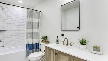 A bathroom with a white bathtub, a toilet, a shower curtain, a sink with a mirror, and a cabinet.