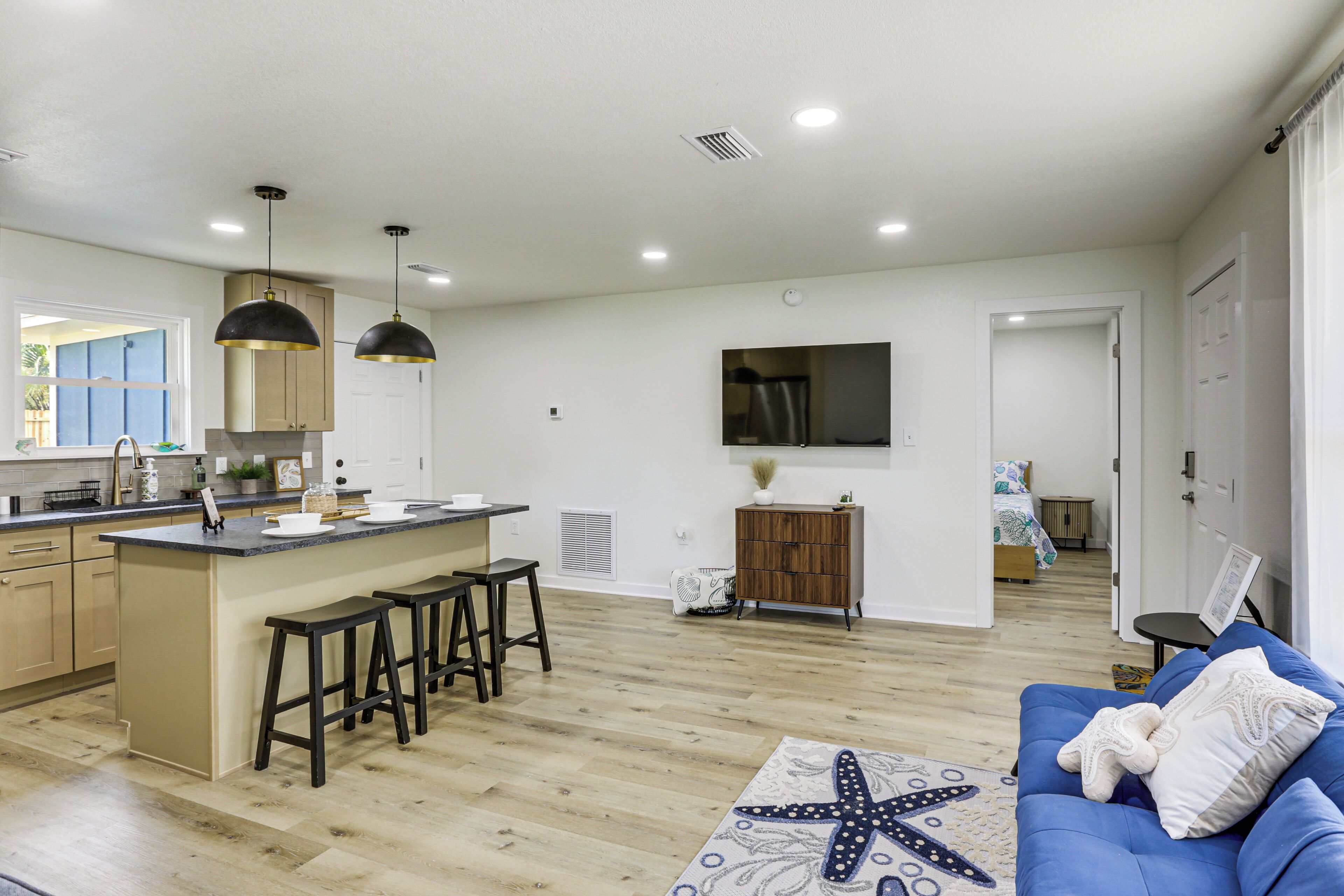 A modern kitchen with a central island, bar stools, a dining area with a blue sofa, and a starfish-patterned rug.