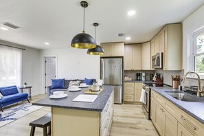 Uma cozinha moderna com ilha central, eletrodomésticos de aço inoxidável e um sofá azul na área de estar adjacente.