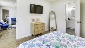 Un dormitorio con cama, tocador, televisor y baño a la vista a través de una puerta abierta.