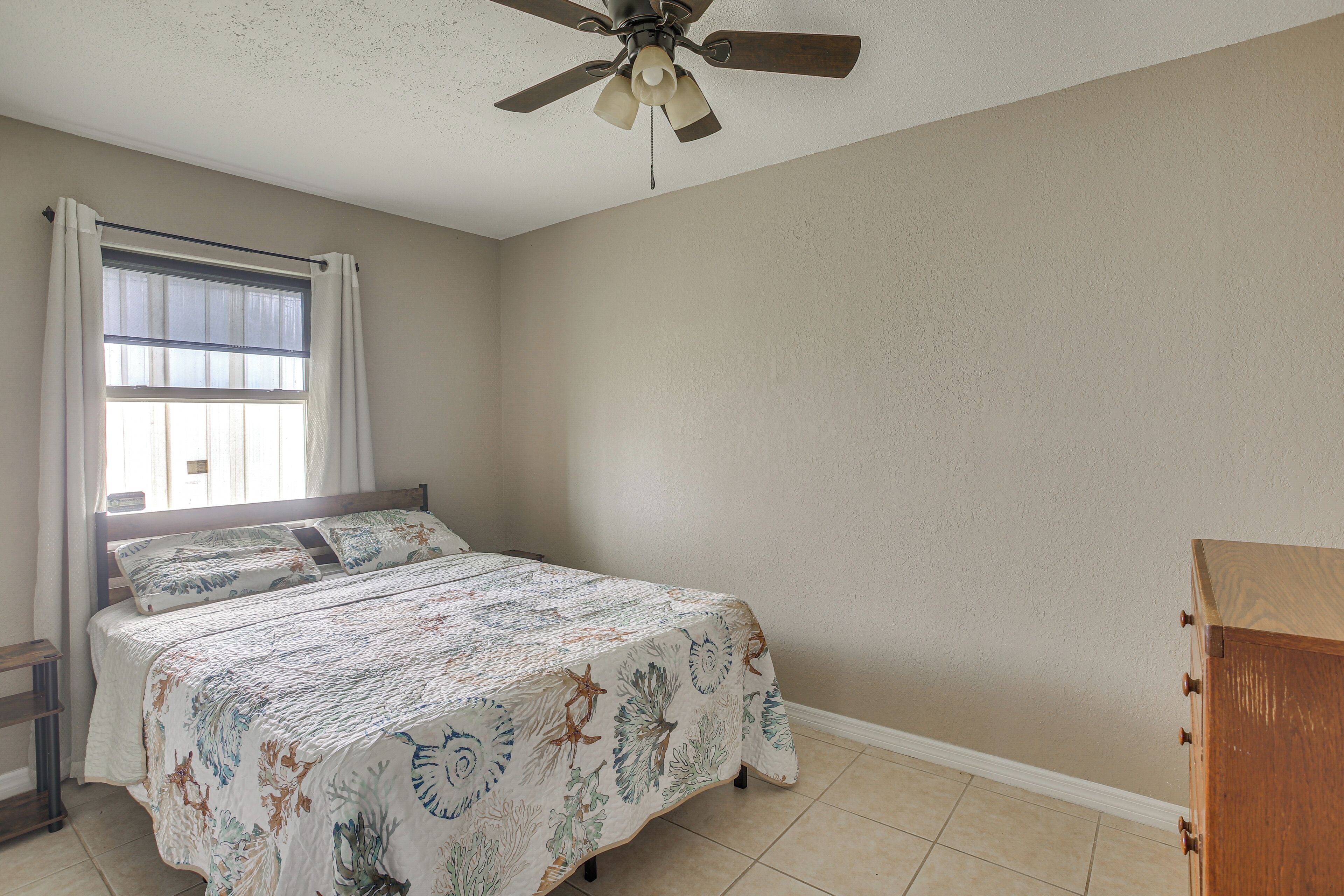 A bedroom with a bed, a ceiling fan, a window with curtains, and a wooden dresser.