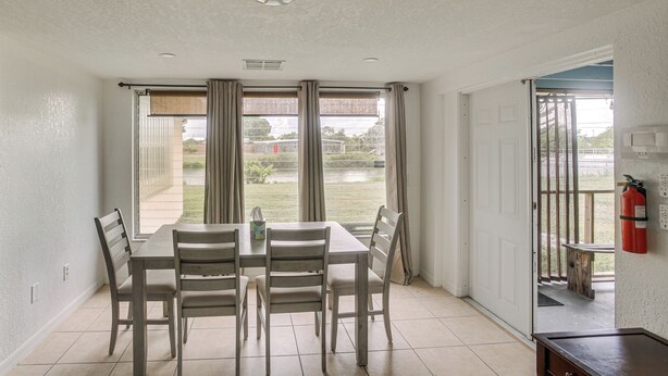 Un comedor con mesa y sillas, ventanas amplias con cortinas, un extintor y vistas al exterior.
