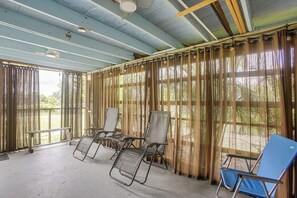 A covered outdoor seating area with metal chairs and a bench, large windows with curtains, and a concrete floor. - 4 Mi to Beach Park! Canal-front Port Charlotte Gem (Port Charlotte)