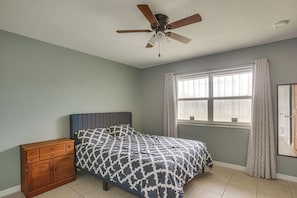 Ein Schlafzimmer mit einem Bett, einem Deckenventilator, einem Fenster mit Vorhängen und einer Holzkommode.