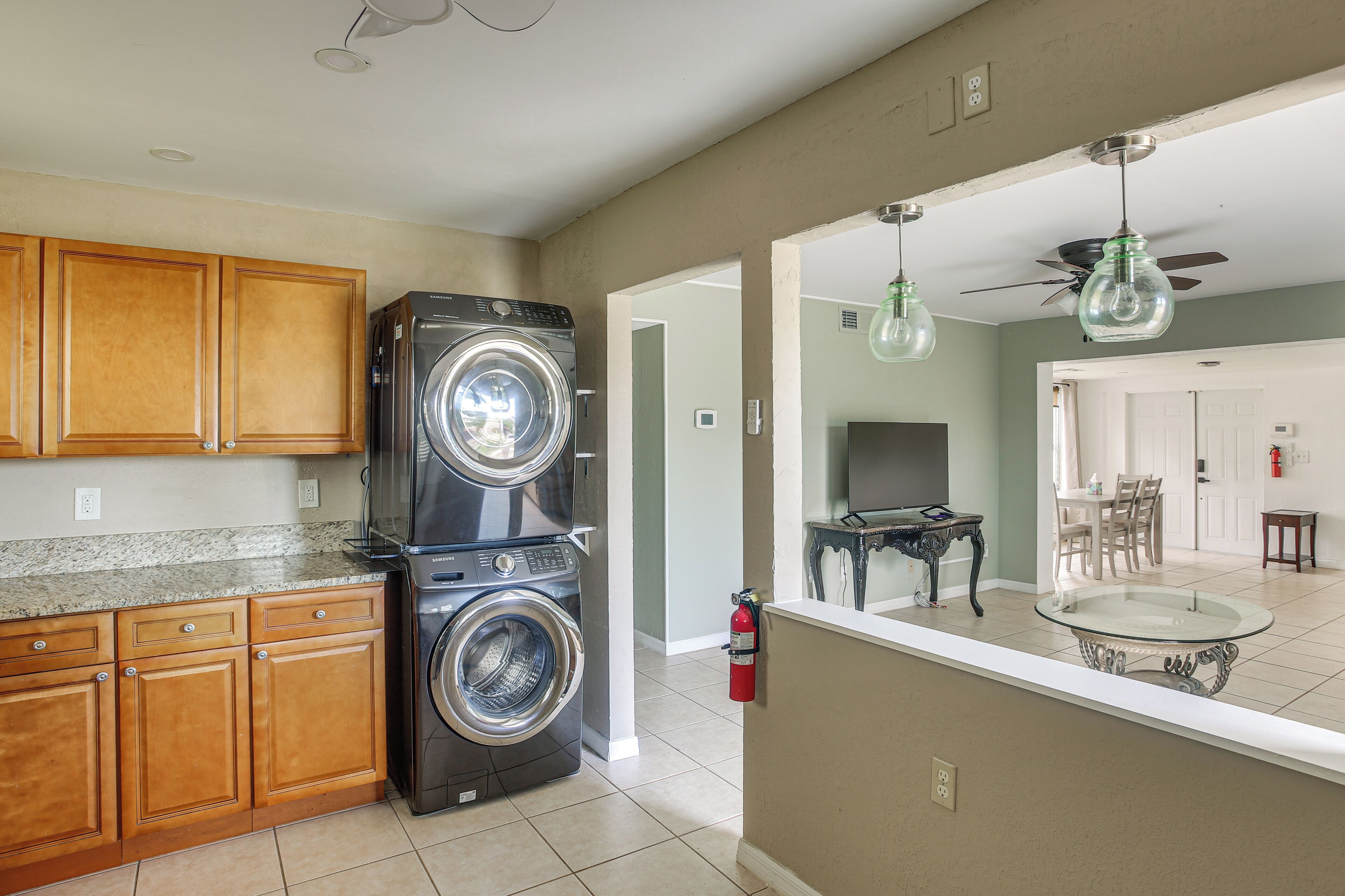 A kitchen with wooden cabinets, a washing machine, a dining area with a table and chairs, and a ceiling fan.