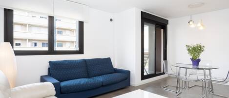 A modern living room with a sofa, a coffee table, a dining table with chairs, a potted plant, and a view of the outside.