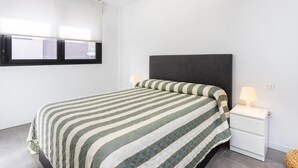 A bedroom with a bed, a nightstand, a wall-mounted TV, and a window with blinds. - CHL Apartamento Confort Güímar, Tenerife (Güimar)