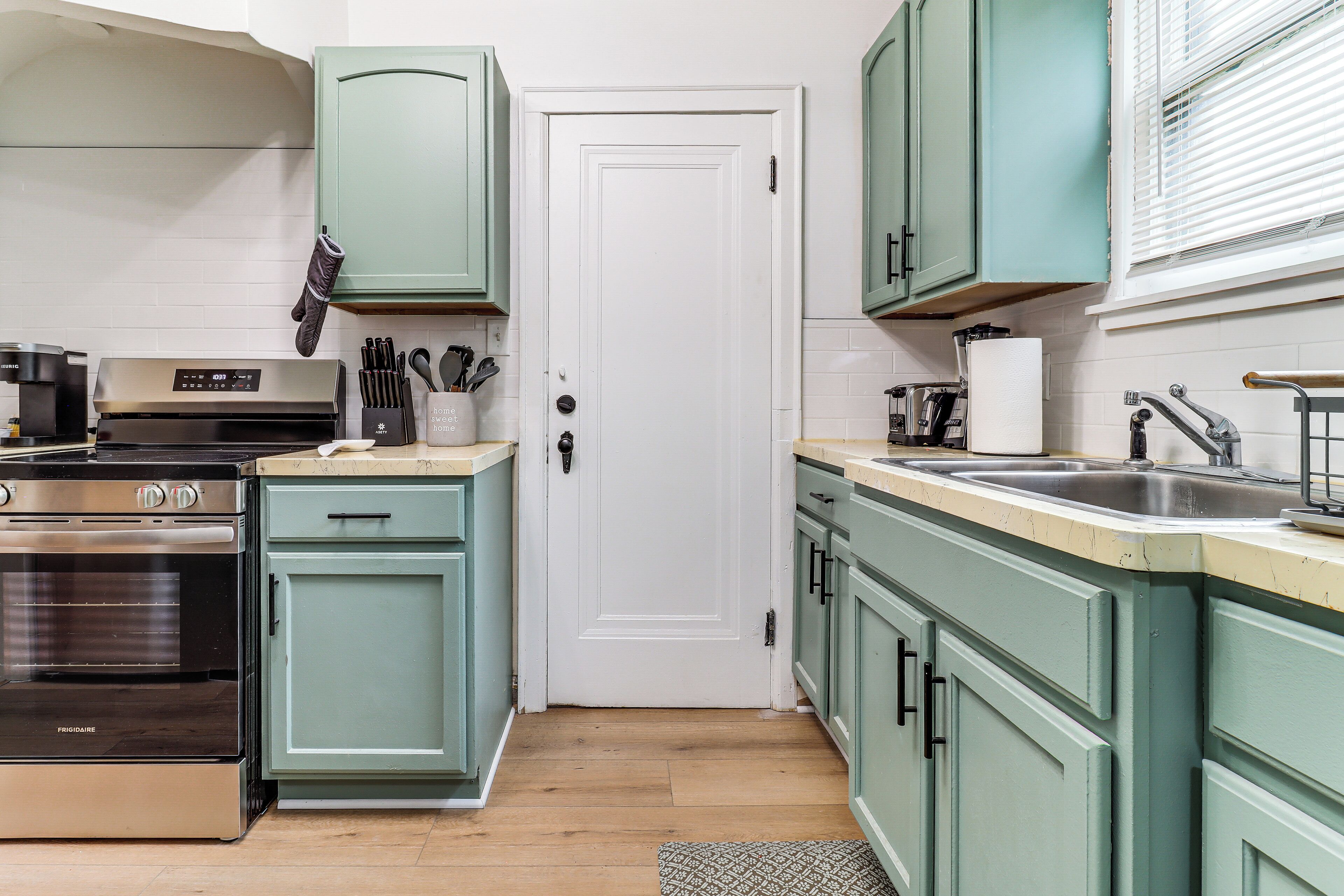 A kitchen with a stainless steel oven, a coffee machine, and teal cabinets.