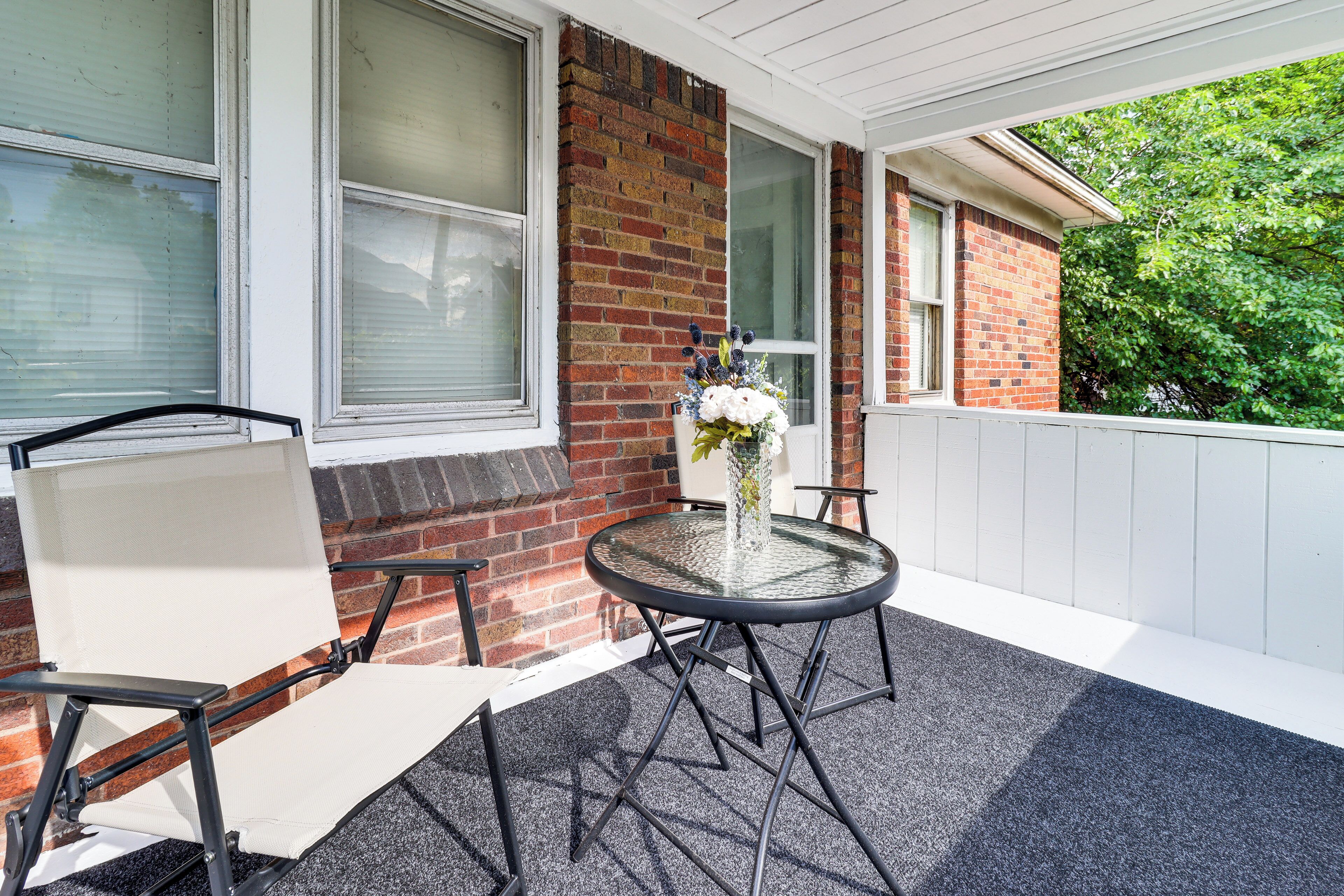 A patio with a round table, two chairs, a vase with flowers, and a brick wall.