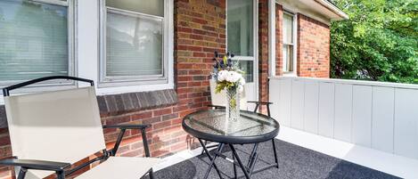 A patio with a round table, two chairs, a vase with flowers, and a brick wall.