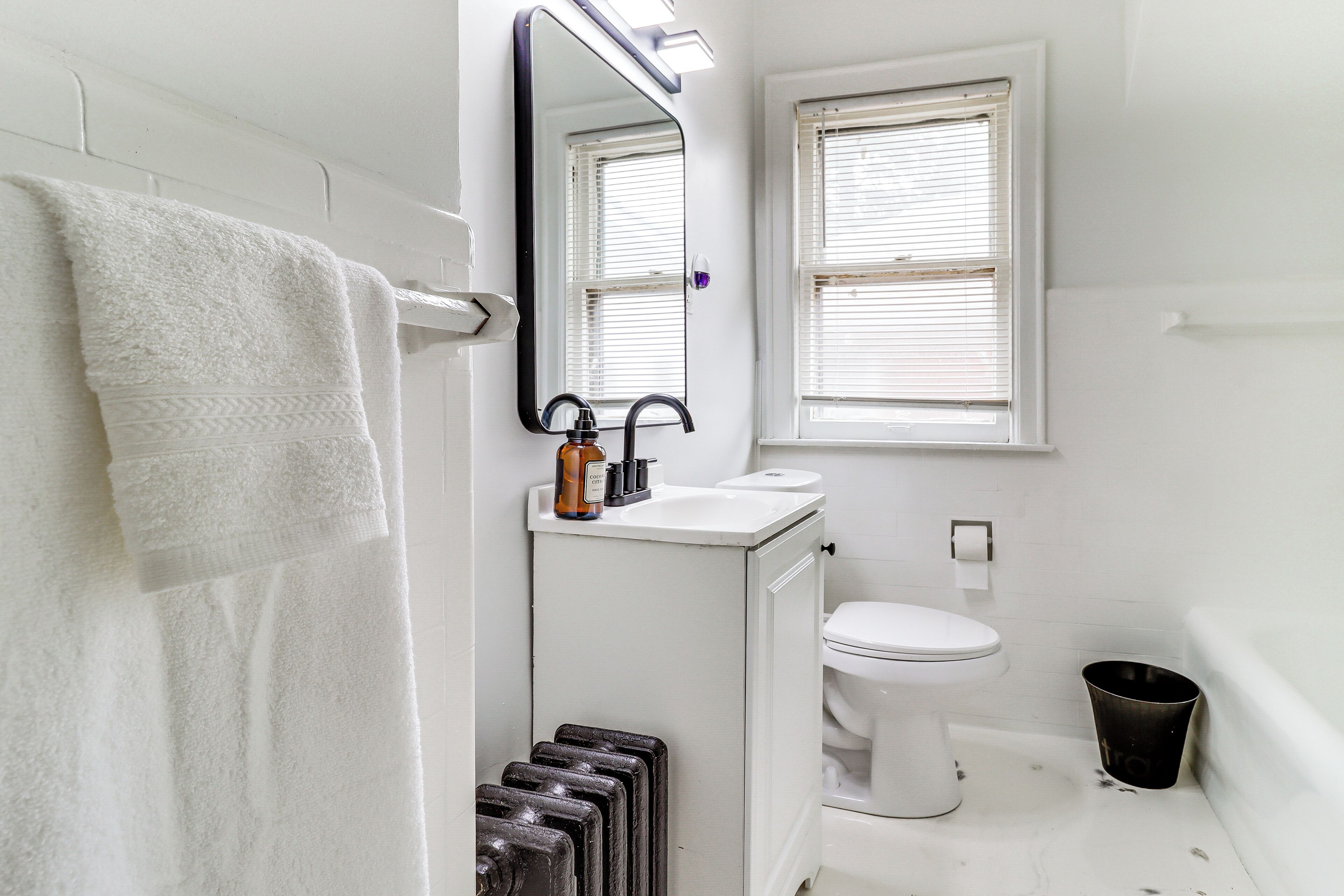 Ein Badezimmer mit Waschbecken, Toilette, Spiegel und einem Fenster mit Jalousien.