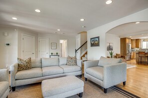 Una sala de estar con un conjunto de sofás, una mesa de centro y una escalera que lleva a una cocina.