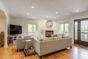 Una sala de estar con sofá, televisor, chimenea y ventanas amplias.