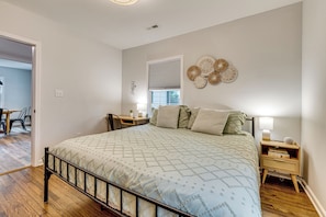A bedroom with a bed, bedside tables, a window with blinds, and a wall decoration.
