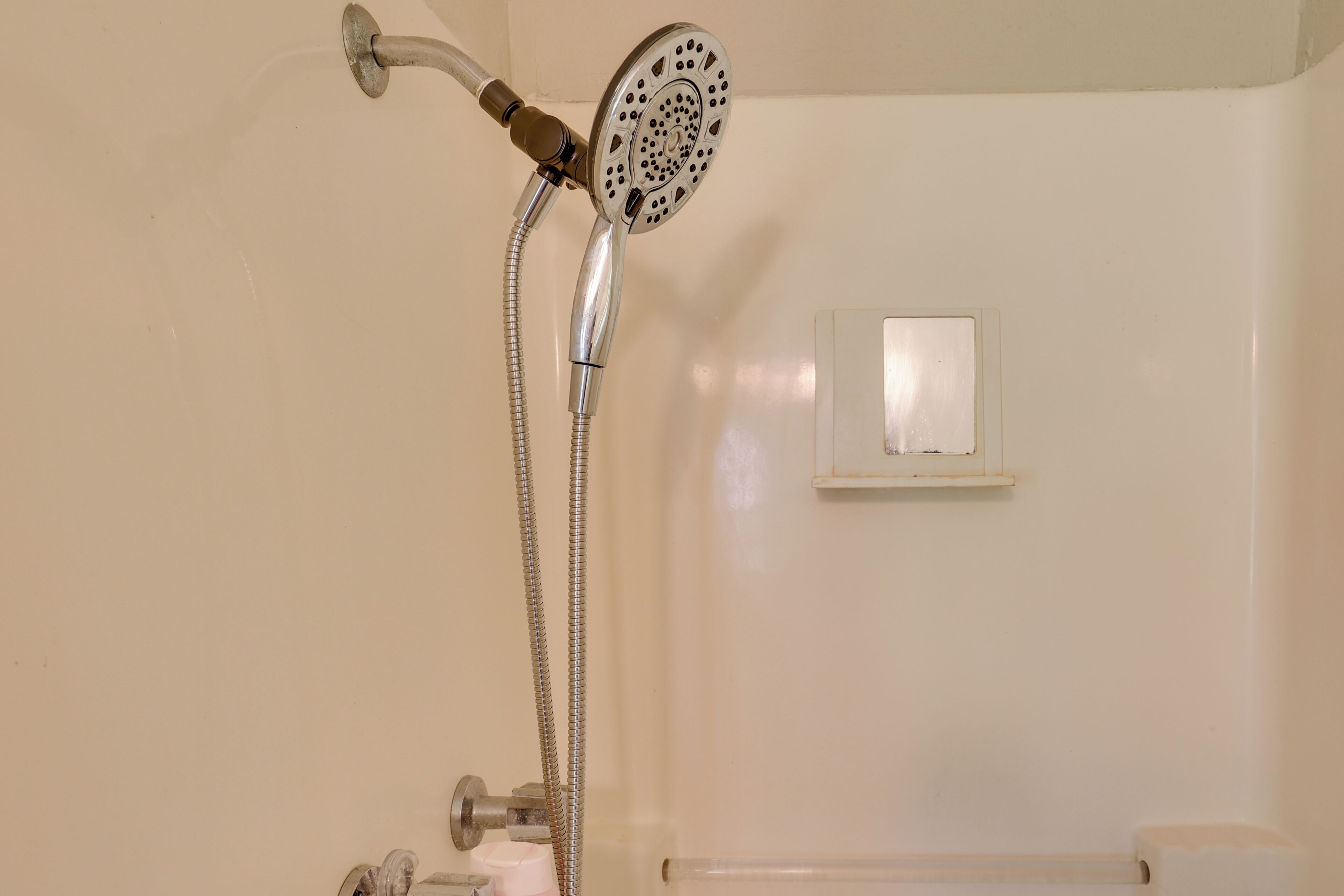 Een douche met een handdouche en een bedieningspaneel aan de muur.
