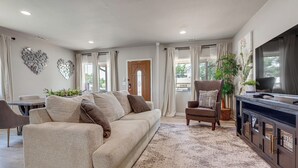 A living room with a sofa, armchair, TV stand, and decorative wall art.