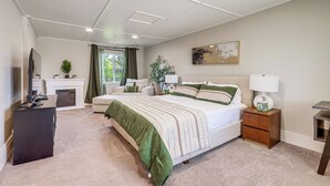 A bedroom with a bed, bedside tables, a dresser, a TV, a fireplace, and a window with curtains.
