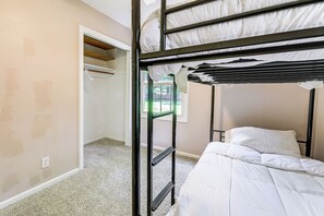 Ein Etagenbett mit weißer Bettwäsche, ein Schrank mit Spiegel und ein Fenster mit Blick auf Grünflächen.