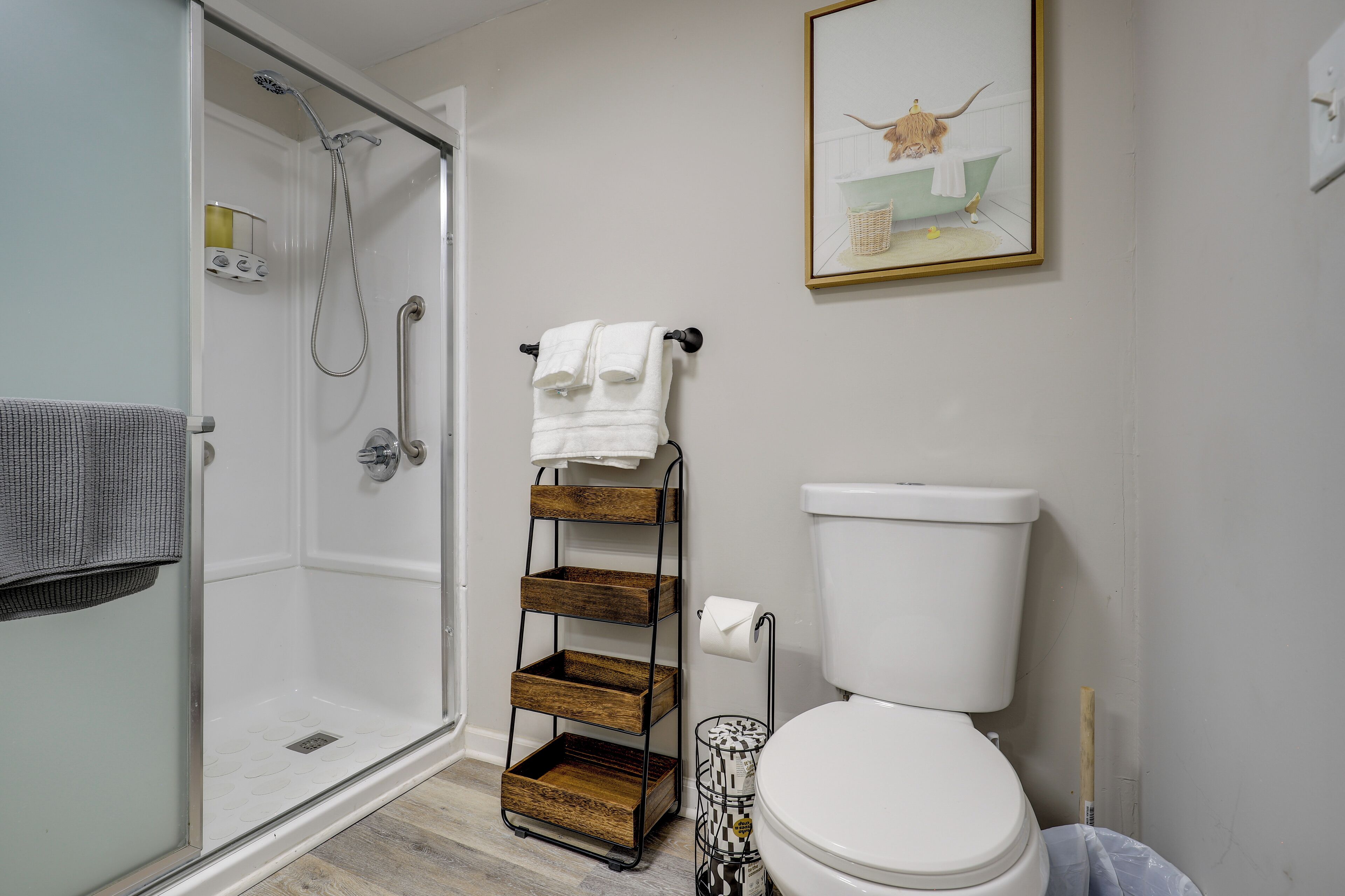A bathroom with a glass-enclosed shower, a toilet, a towel rack, and a framed picture on the wall.
