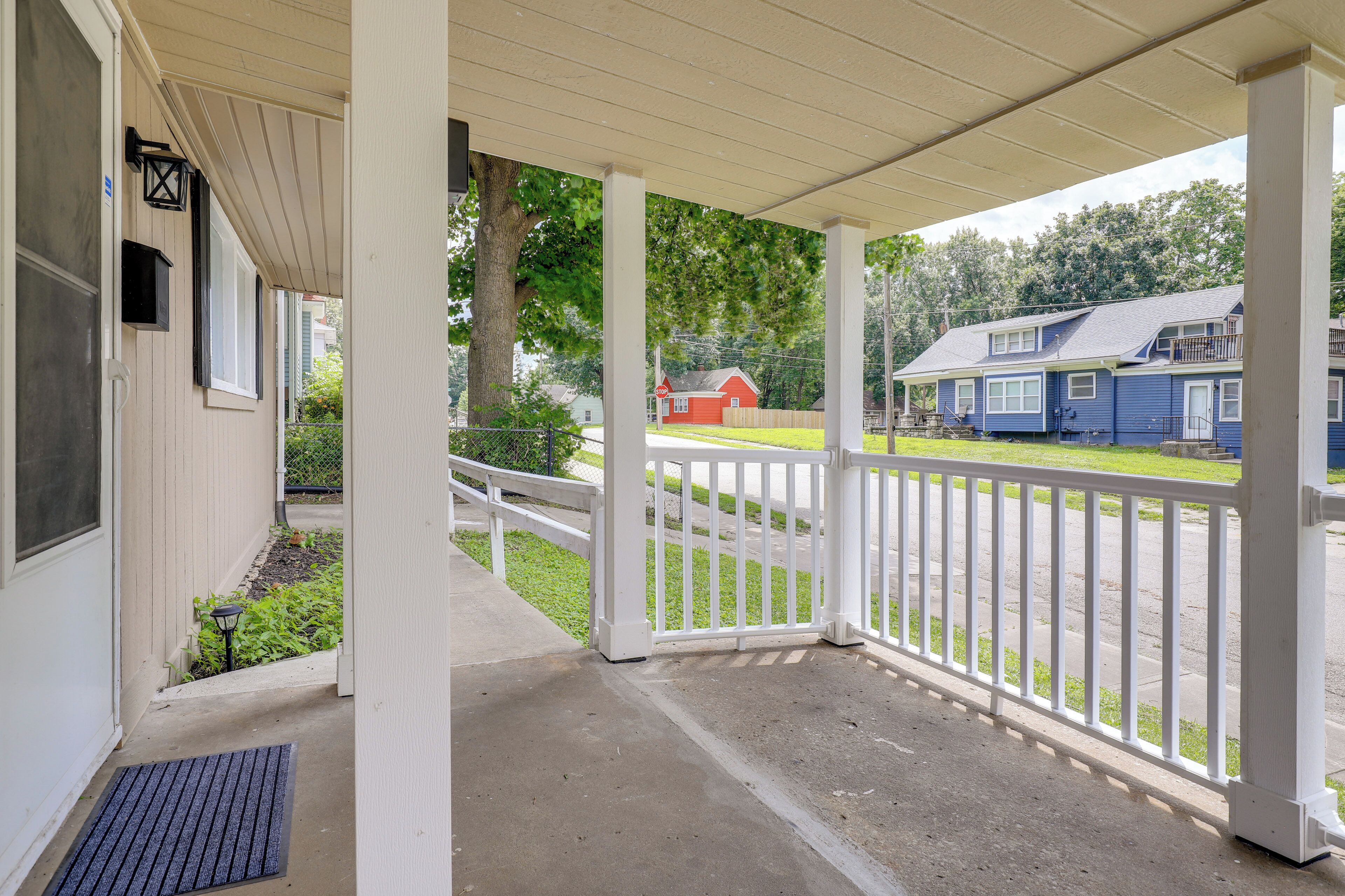 A covered porch with a white railing, a concrete floor, and a view of a street with houses.