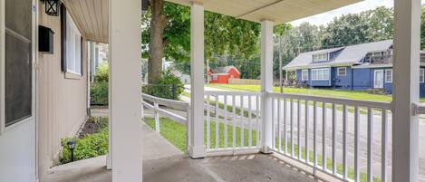 A covered porch with a white railing, a concrete floor, and a view of a street with houses.