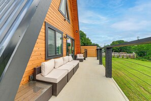A modern outdoor seating area with a wooden deck, cushioned benches, and a view of a green lawn. - A Frame Family Escape With Water Views (Little Elm)