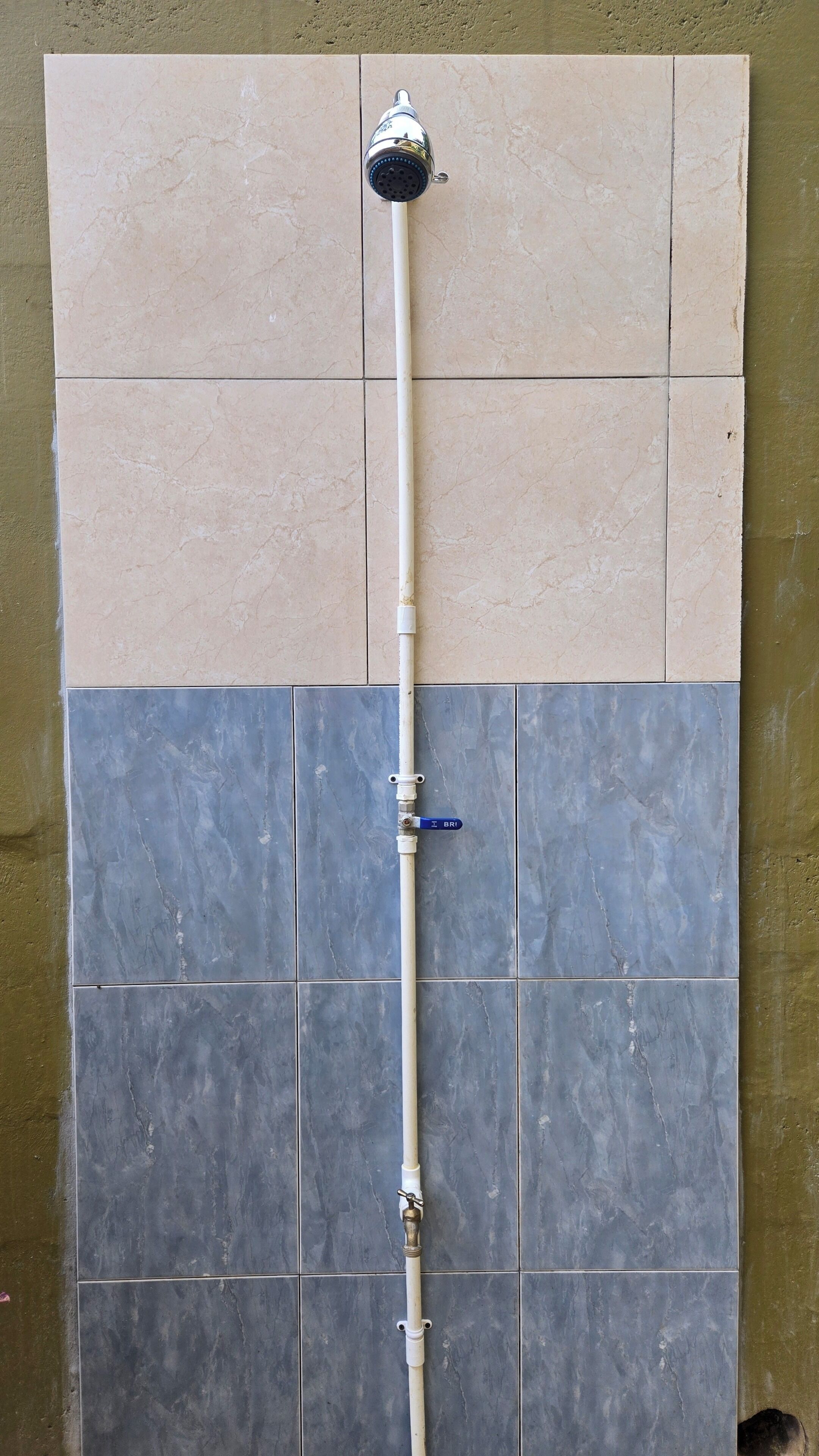A shower with a chrome head and a white pipe against a tiled wall.