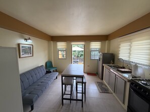 Ein kompakter Wohnbereich mit Sofa, Esstisch, Küchenzeile und Blick ins Freie.