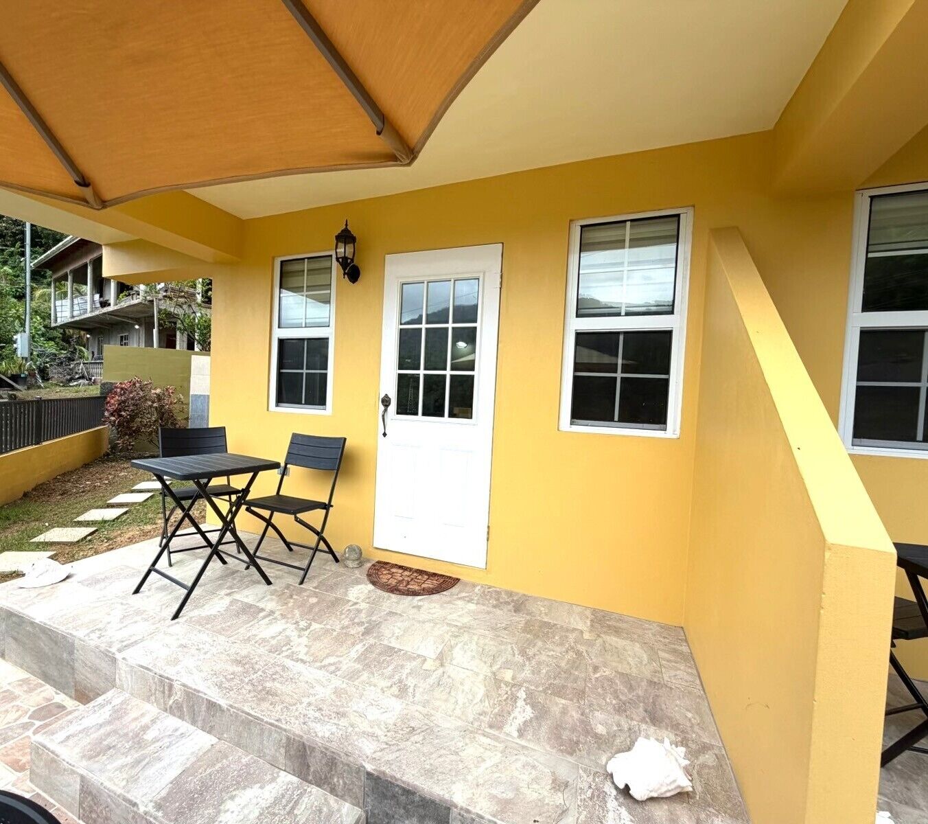 Fachada amarela com porta, janelas e um pátio com mesa e cadeiras.