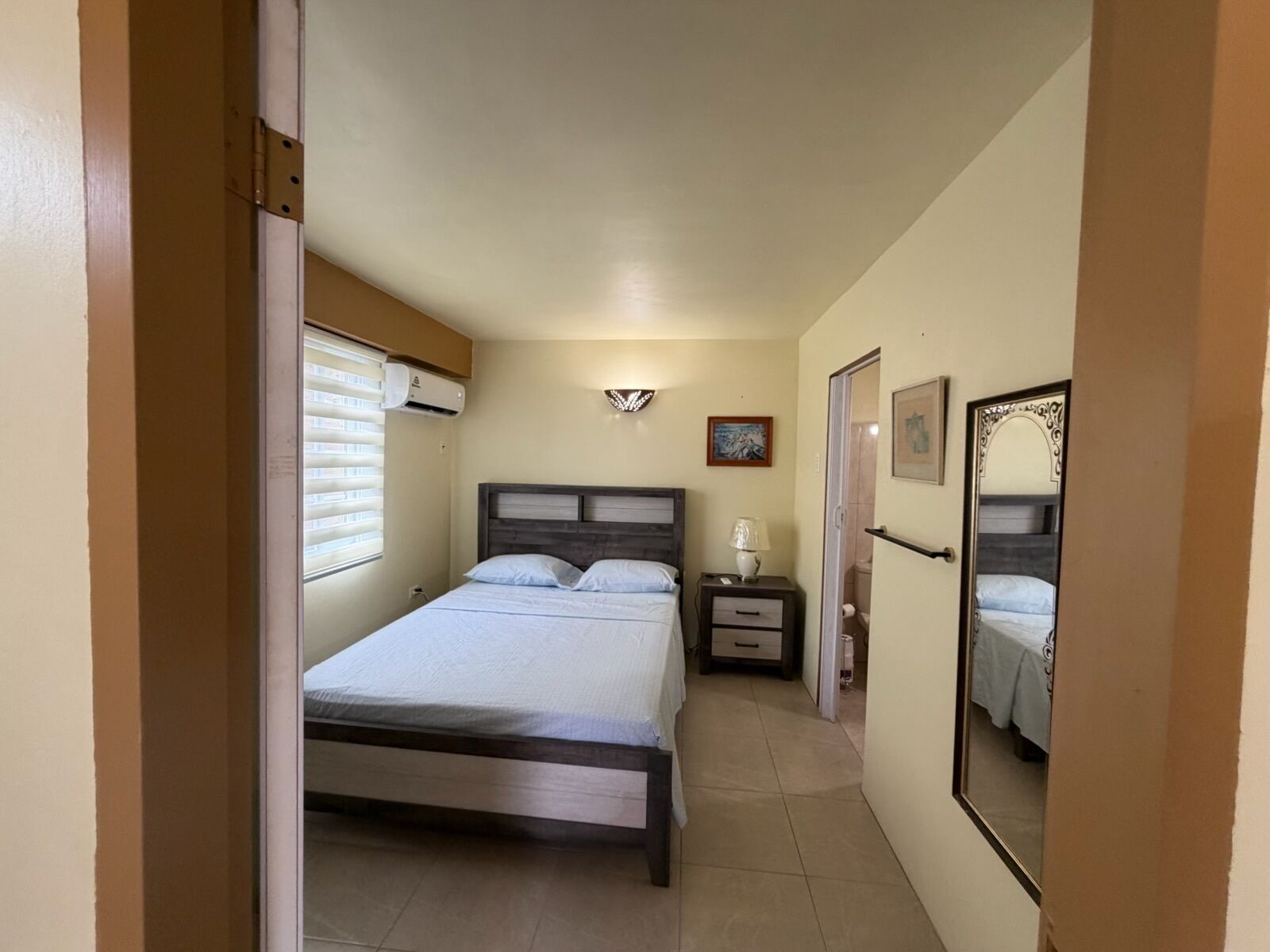 A bedroom with a bed, bedside table, lamp, and a mirror.